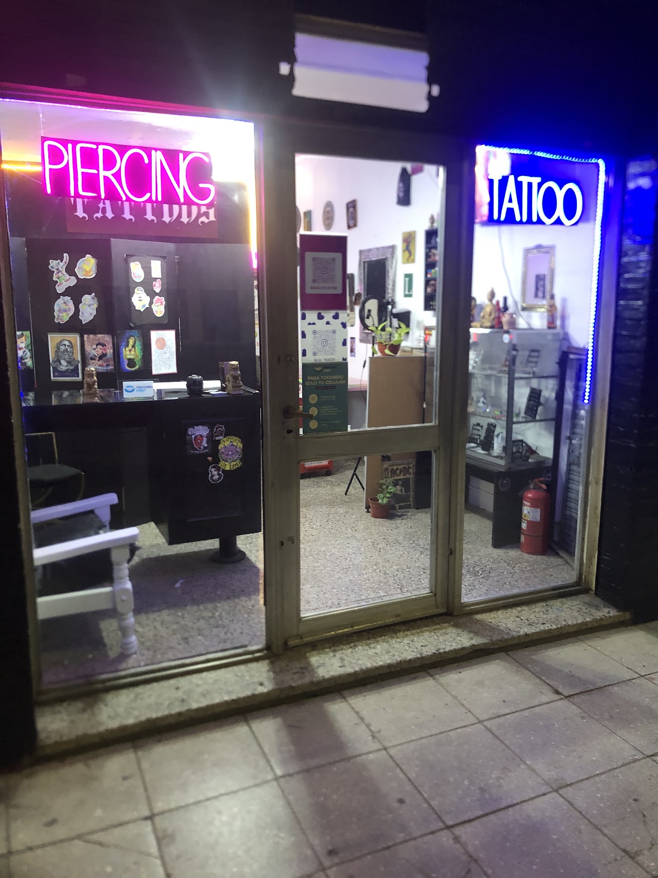 Fachada nocturna de Santos Tattoos con carteles de neón de Piercing y Tattoo iluminados en Berazategui